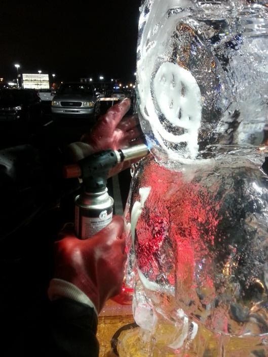 Firefighter using a hose to spray water at a large ice sculpture at night