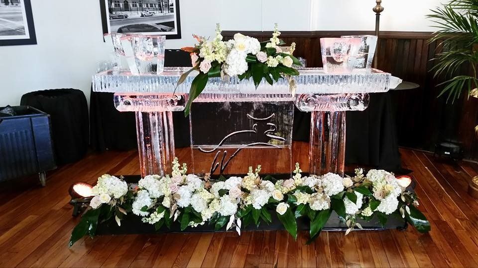 Decorated glass table with white floral arrangements and greenery on a polished wooden floor indoors