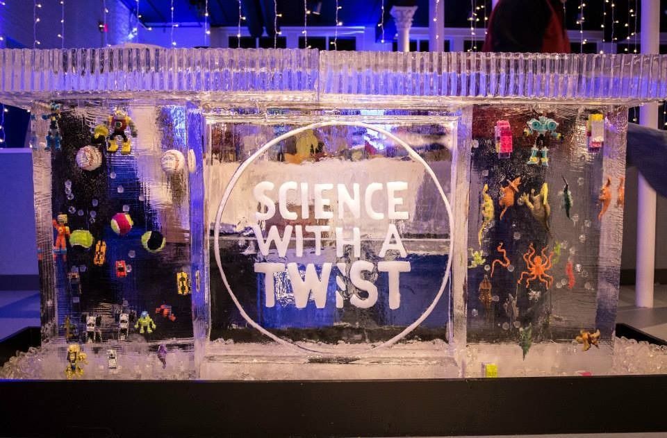 A festive display with “SCIENCE WITH A TWIST” sign, lit by blue and gold lights and surrounded by decorations
