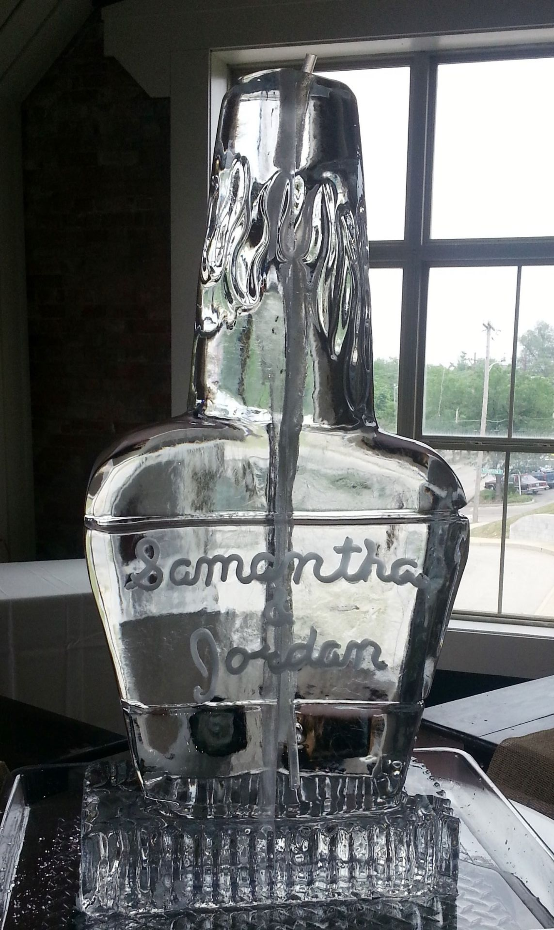 Clear glass bottle on a counter with water pouring from the top, in front of a window.