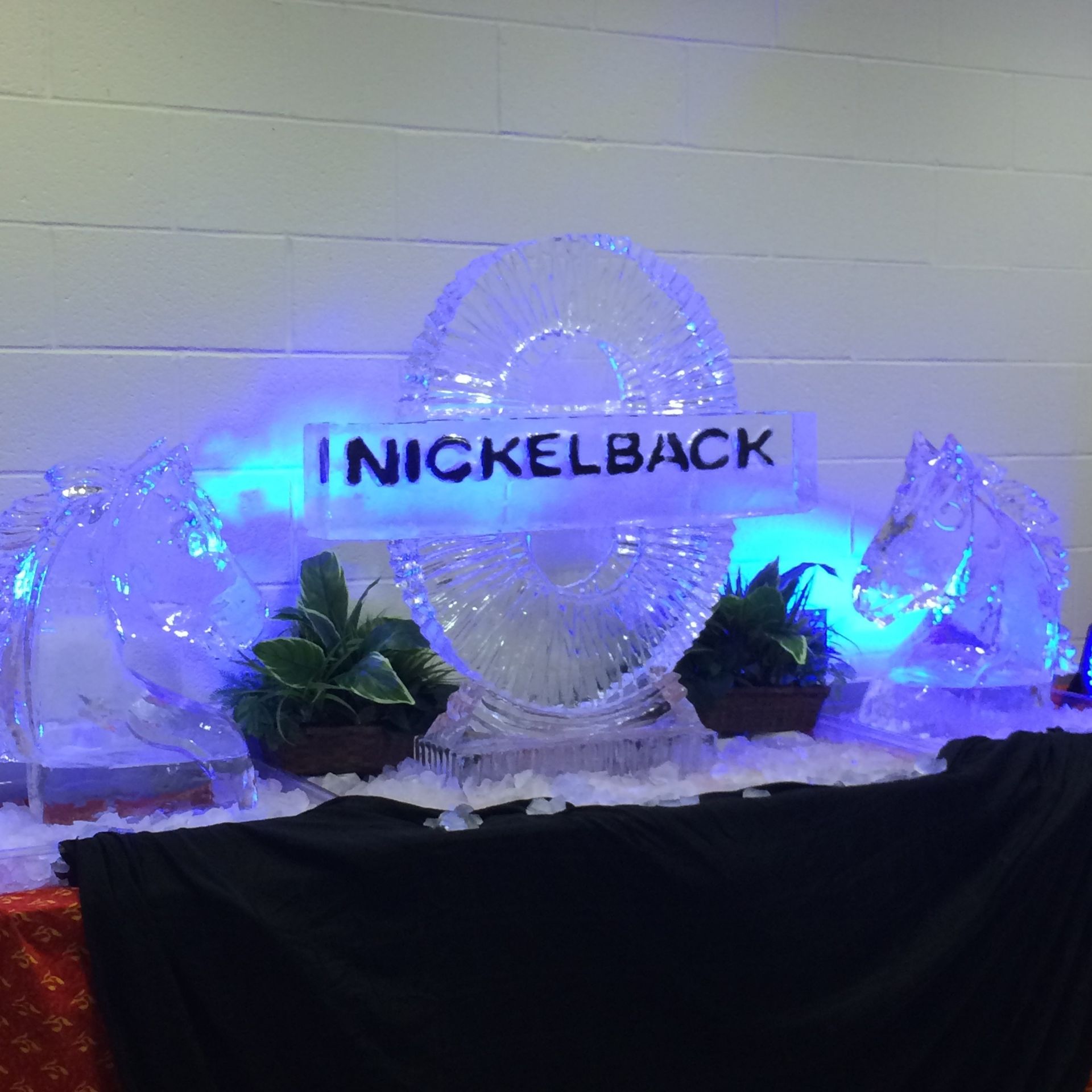 Illuminated Nickelback display with blue lights, ice sculptures, and plants on a draped table