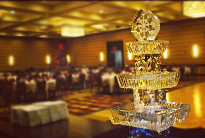 Crystal champagne fountain in a warmly lit banquet hall with tables and guests in the background
