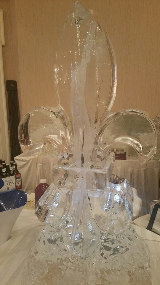 Clear ice sculpture centerpiece with a tall flame-like shape and curved side loops on a table indoors