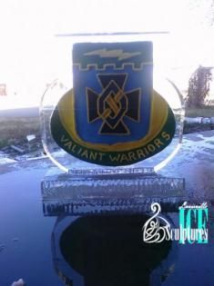 Valiant Warriors crest on a blue shield displayed on a reflective pedestal outdoors