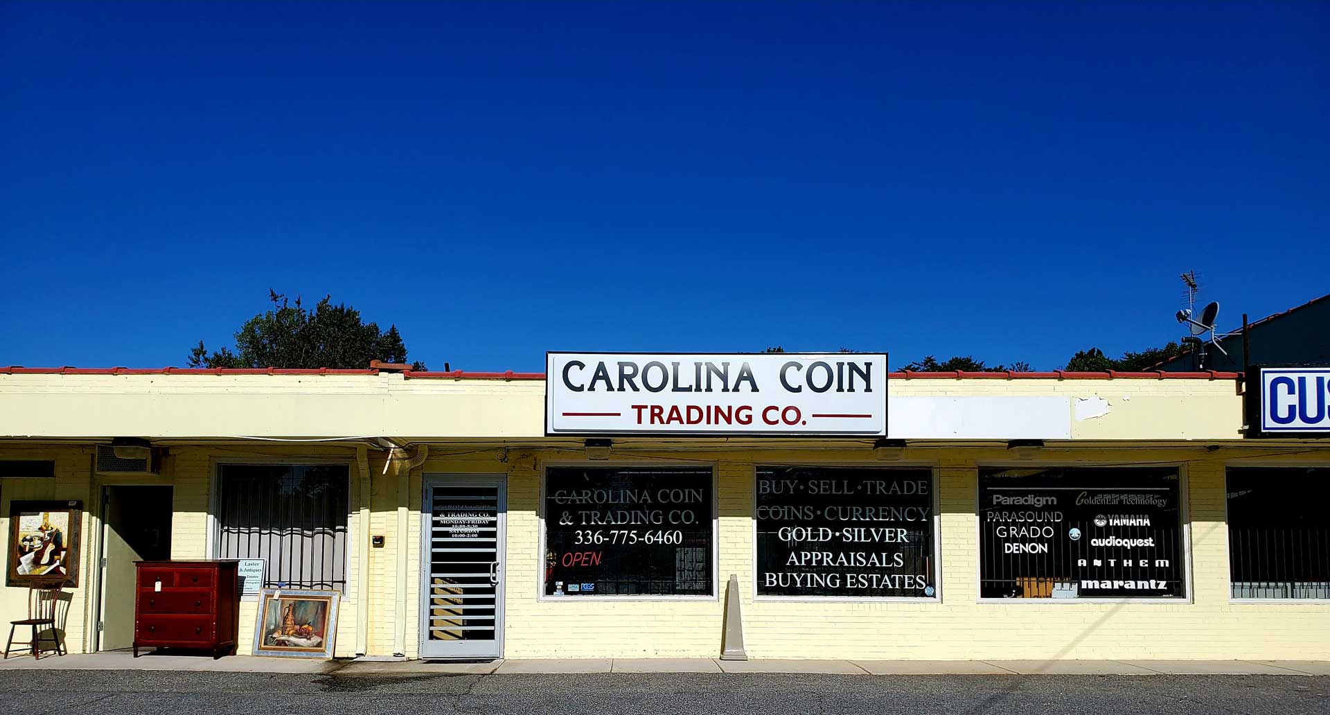 Carolina Coin storefront under a bright blue sky. Light yellow building with multiple display windows.