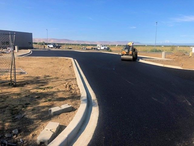 Asphalt paving road construction with roller compacting fresh surface.