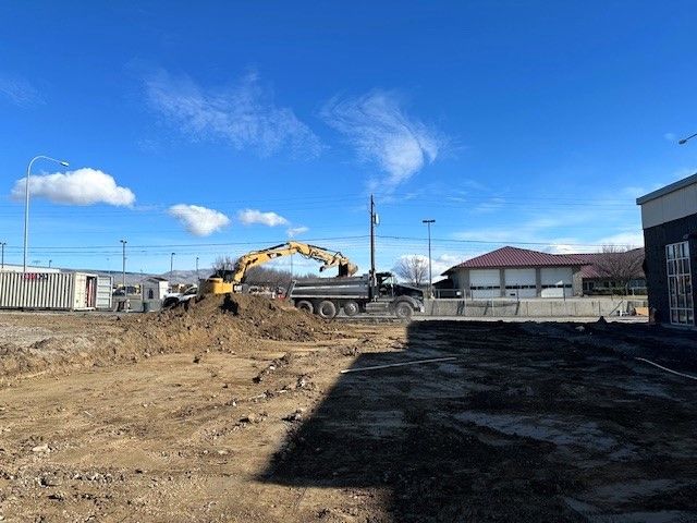 Construction site with excavator loading dirt into a dump truck, under a blue sky.