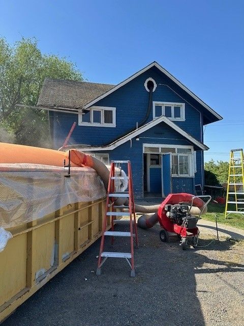 Blue house with debris removal process in progress. A yellow bin, blower, and ladder are set up.