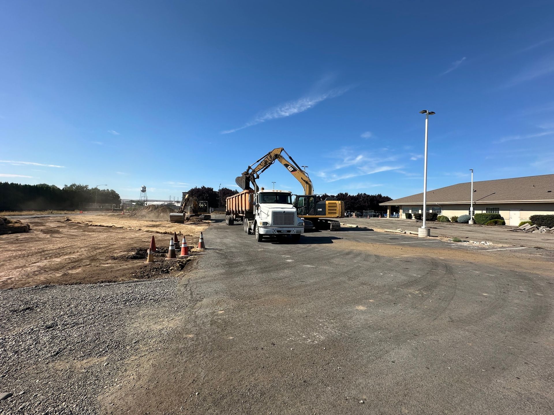 Construction site: Excavator loading logs onto a truck under a blue sky.
