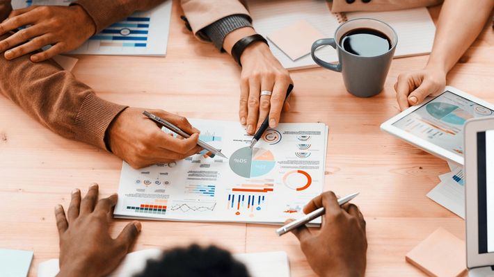 A group of people are sitting around a table looking at graphs, percentages and numbers - Carmen & Co Consulting Strategic Consulting in Southeast Queensland