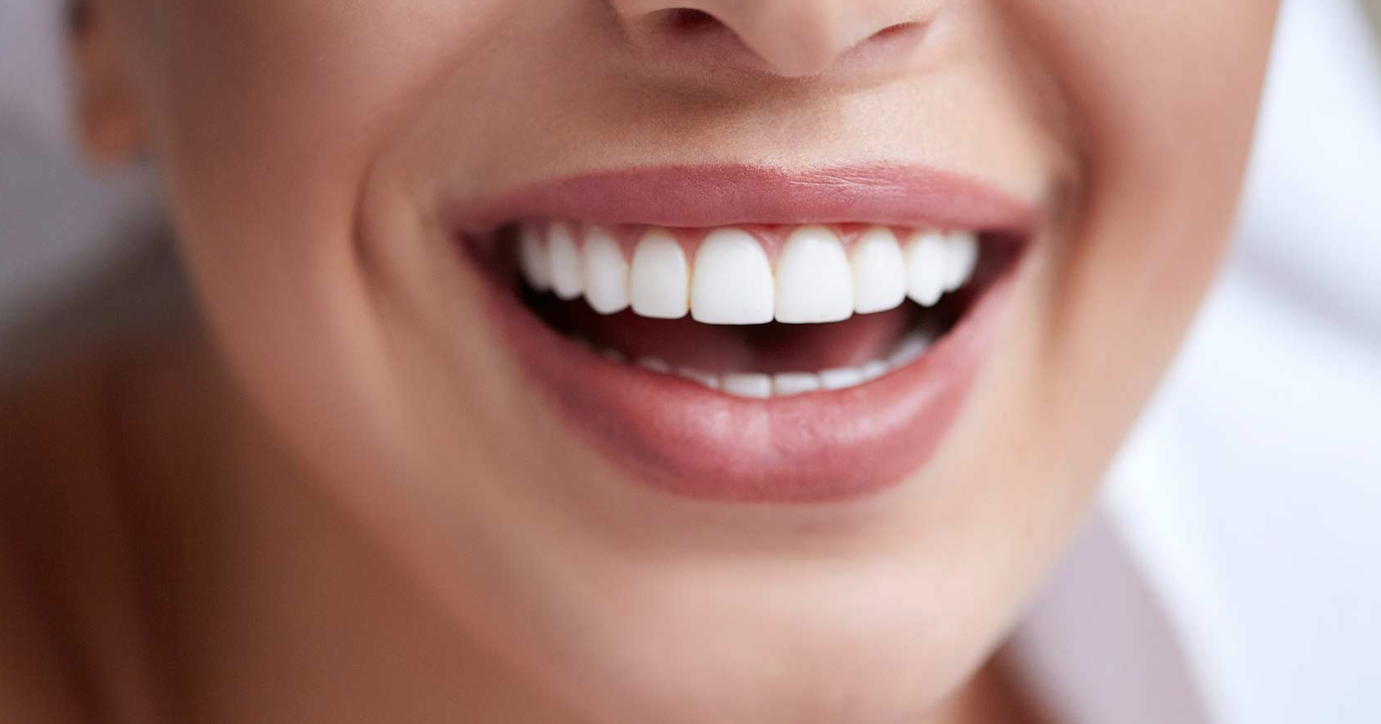 Close-up of a smiling mouth with white teeth and glossy pink lips