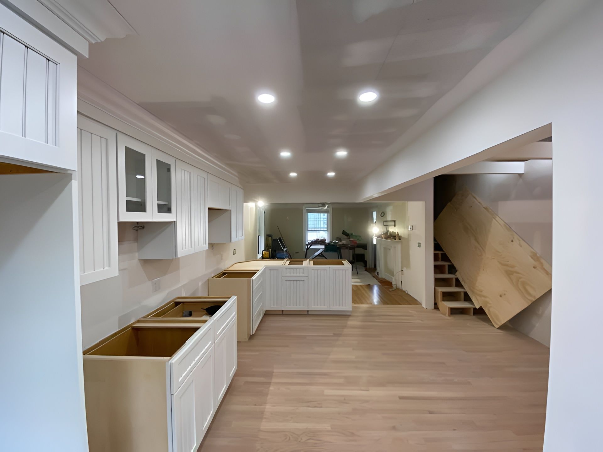 Bright white kitchen with wood floors, island, cabinets, and recessed ceiling lights
