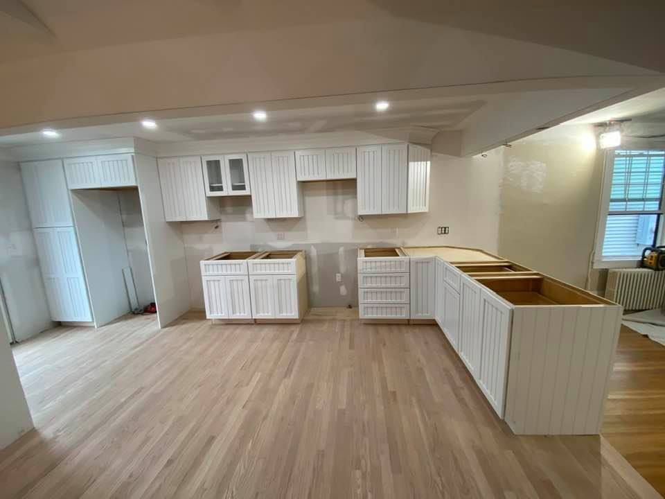 Empty modern kitchen with white cabinets, wood floors, and an island under recessed ceiling lights