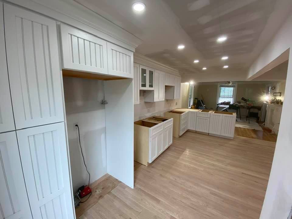 Bright, empty kitchen with white cabinets, wood floors, recessed lighting, and a walk-through opening to another room