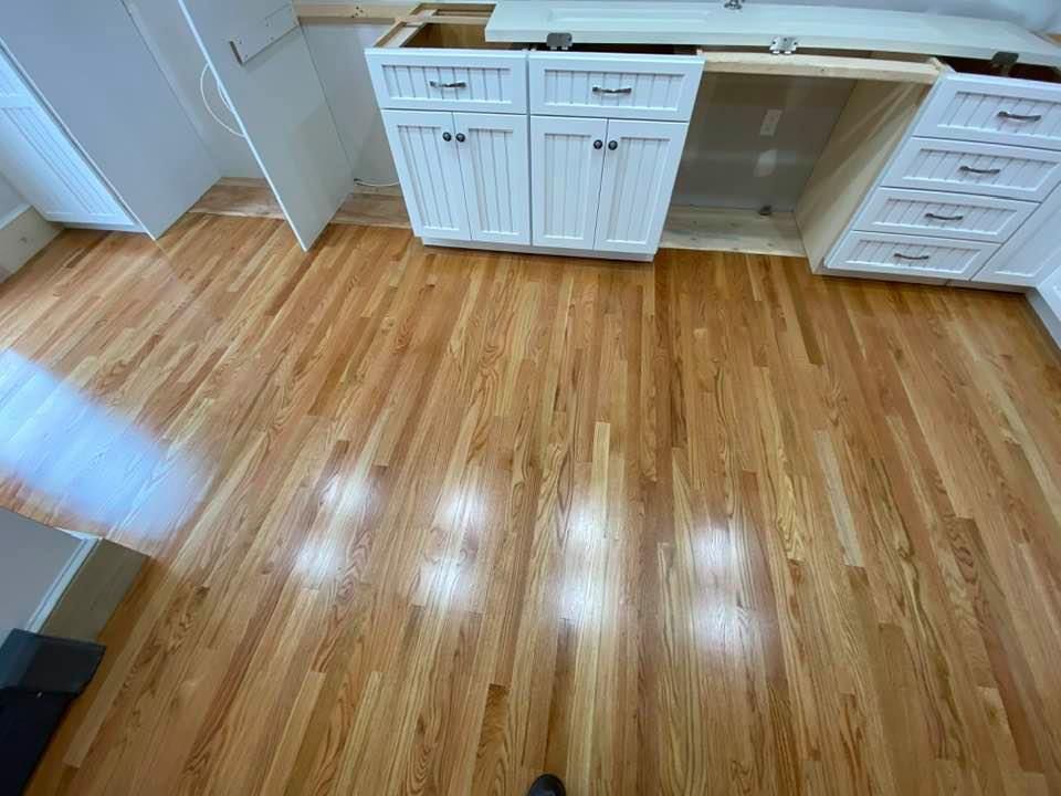 Empty kitchen with glossy hardwood floor and white cabinets under a countertop