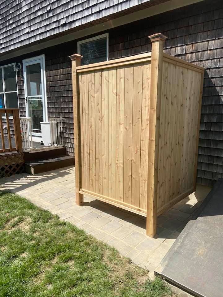 Wooden outdoor storage shed on a patio beside a house, with a small grass lawn nearby.