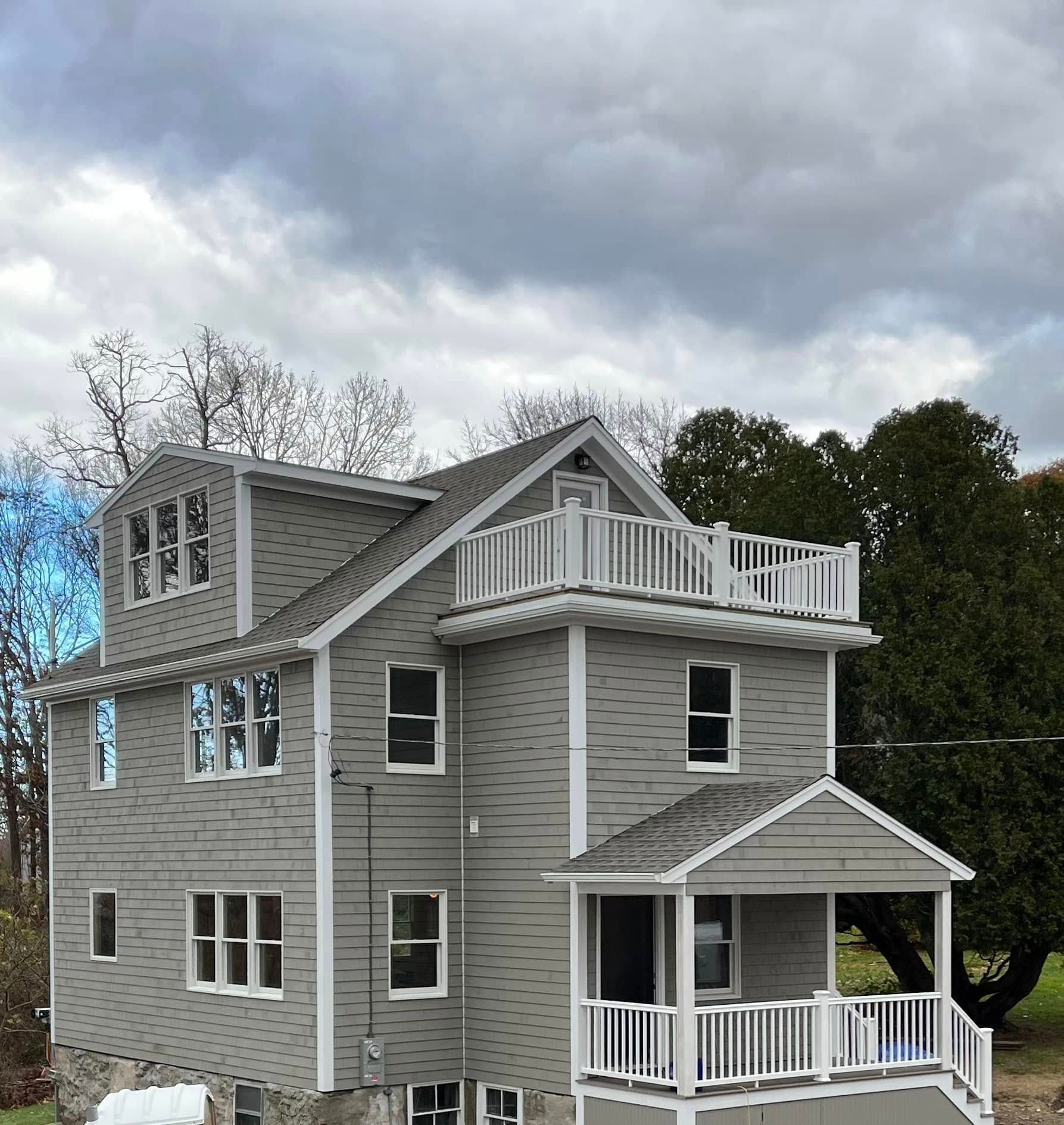 Gray multi-story house with white trim, balconies, and a small front porch under cloudy skies