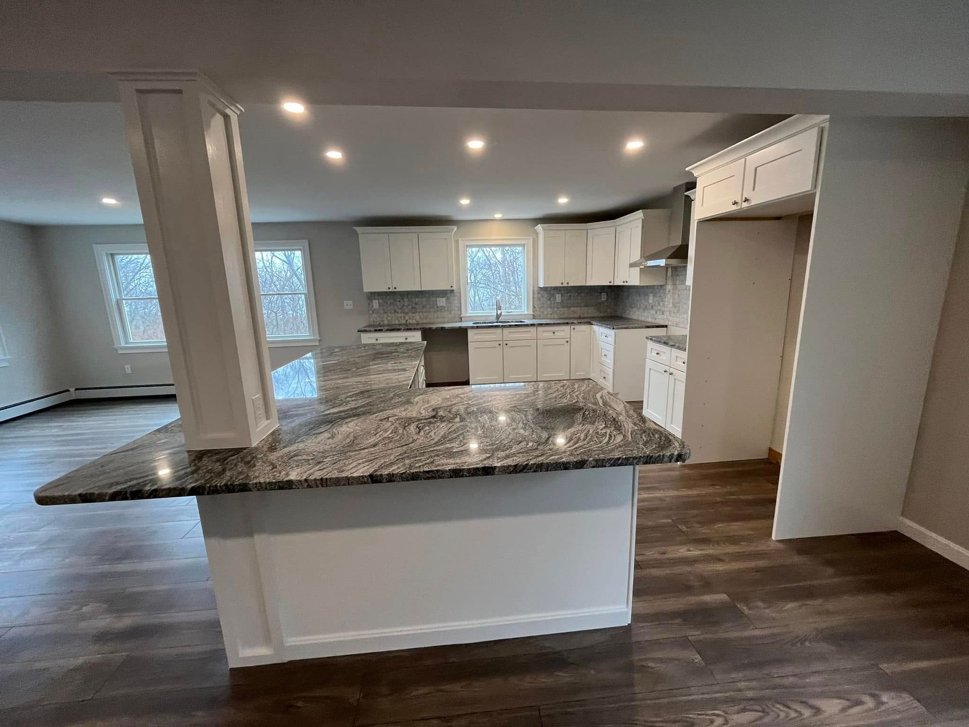 Open-concept kitchen with granite island, white cabinets, and dark wood floors