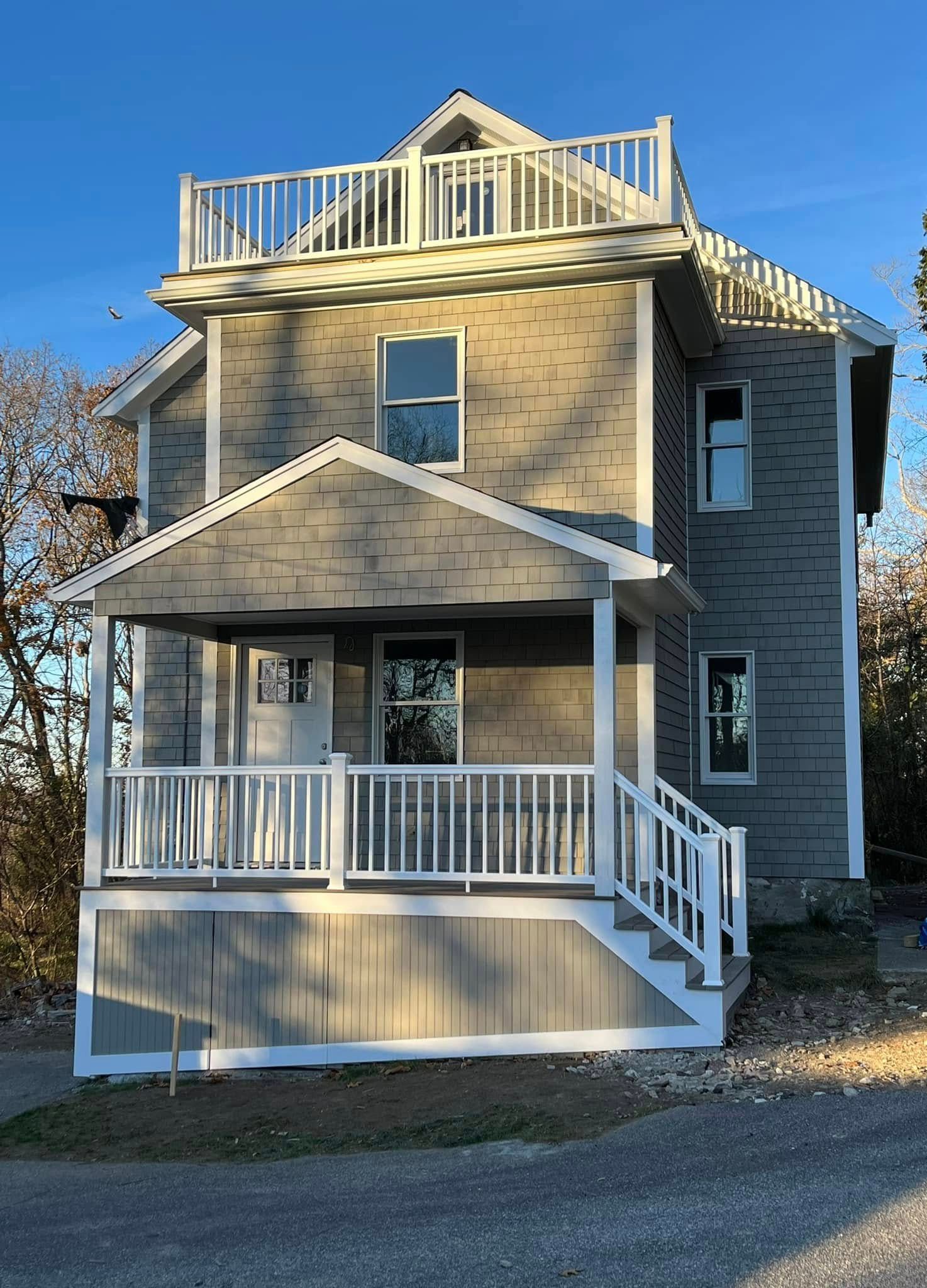 Two-story tan house with white trim, front porch, and rooftop deck under a blue sky