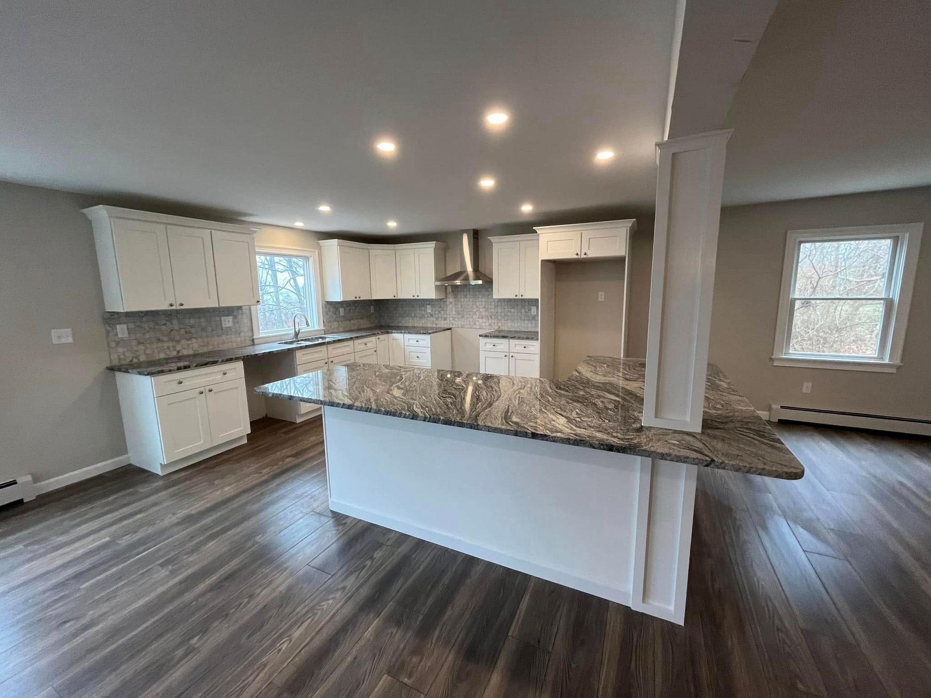 Spacious modern kitchen with white cabinets, gray granite island, and dark wood flooring