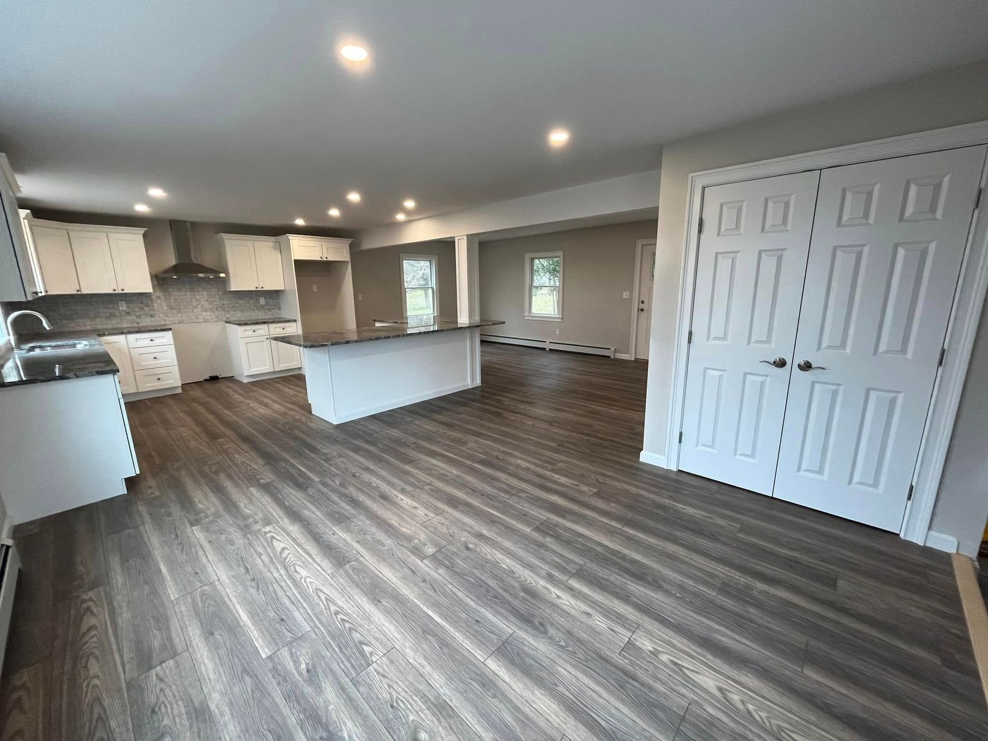 Open-concept kitchen and living area with gray wood flooring, white cabinets, and double closet doors