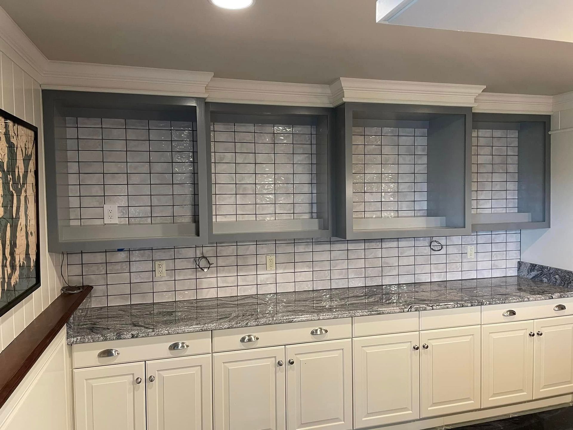 Modern kitchen wall with gray glass-front cabinets, white lower cabinets, and a tiled backsplash