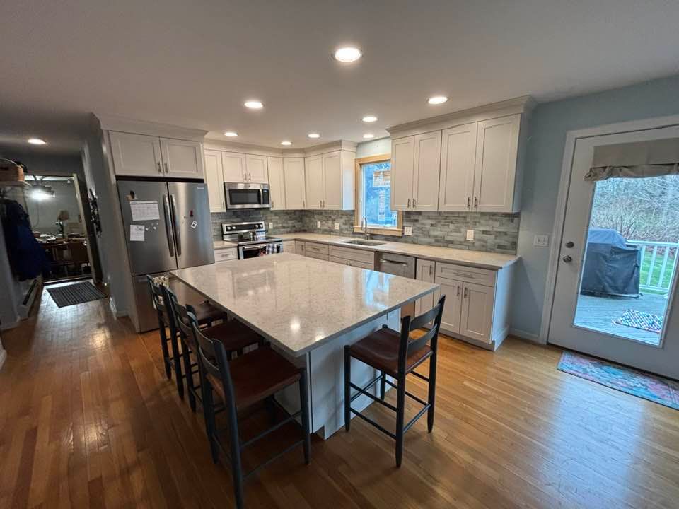 Modern kitchen with white cabinets, large island, stainless fridge, and hardwood floors