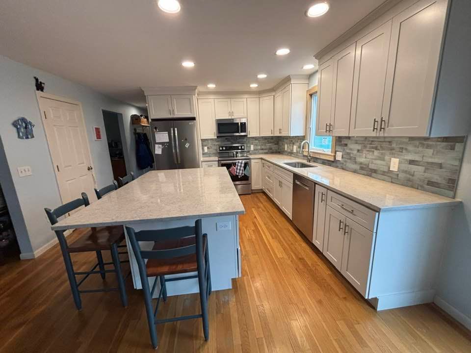 Bright modern kitchen with large island, white cabinets, stainless appliances, and hardwood floors.