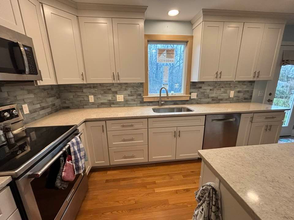 Modern kitchen with white cabinets, gray tile backsplash, stainless appliances, and a window over the sink.