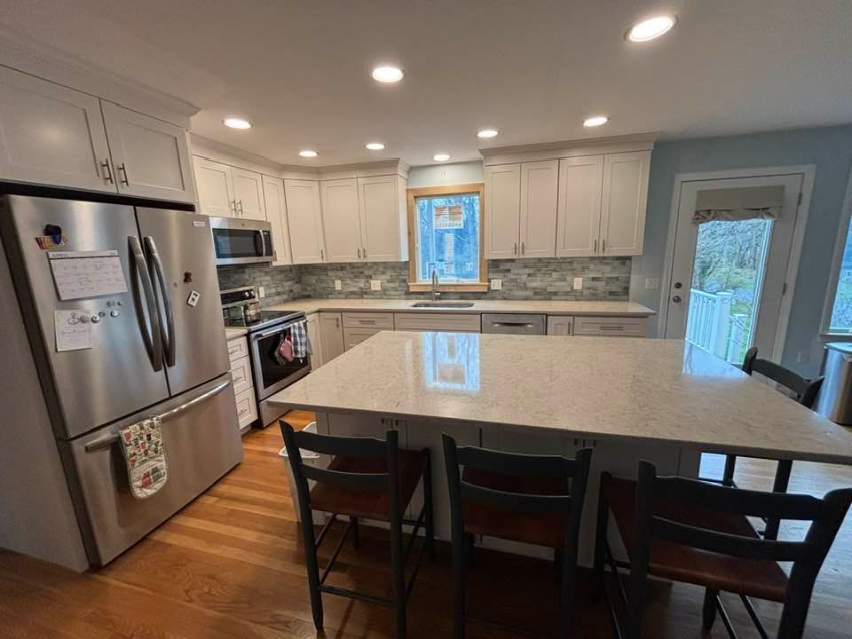 Bright modern kitchen with white cabinets, stainless appliances, island, and black chairs