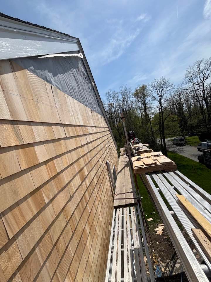 Workers on scaffolding installing siding on a house exterior under a clear blue sky