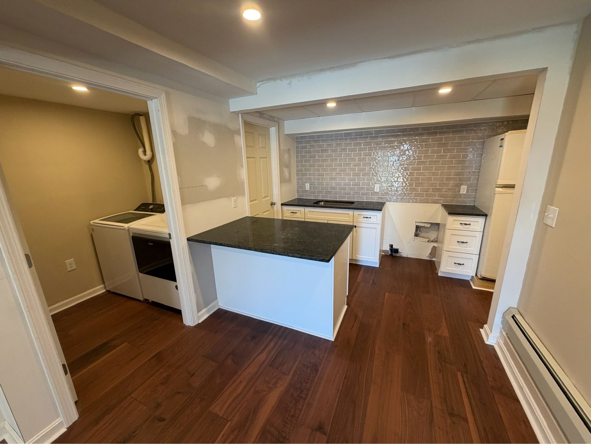 Empty kitchen with white cabinets, dark countertops, and hardwood floors viewed from the dining area.