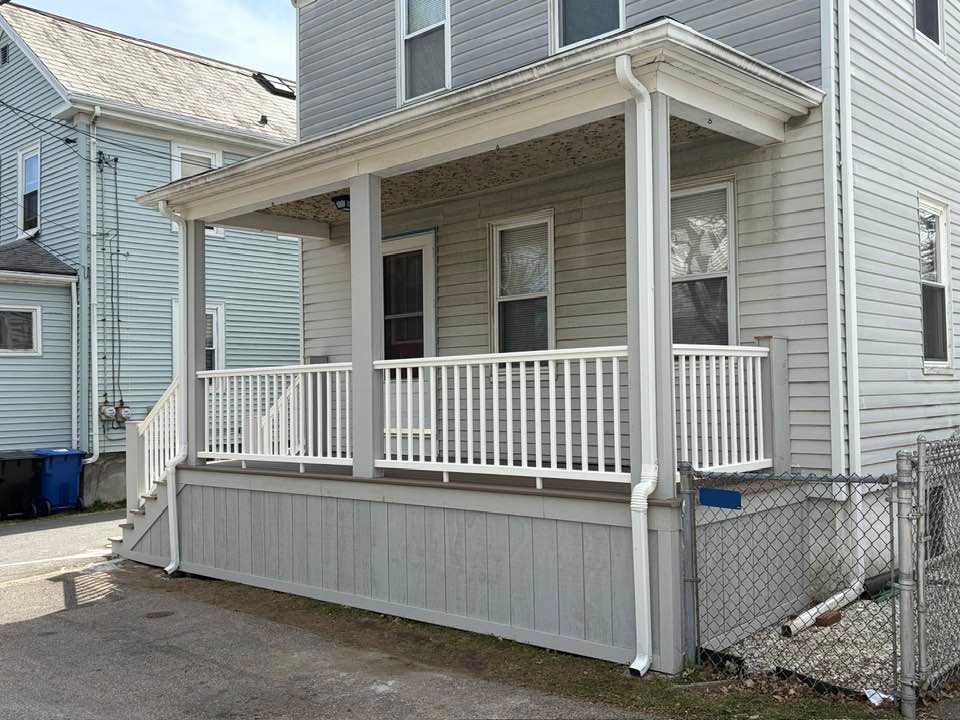 Small gray house with a covered front porch, white railings, and a ramp on the side
