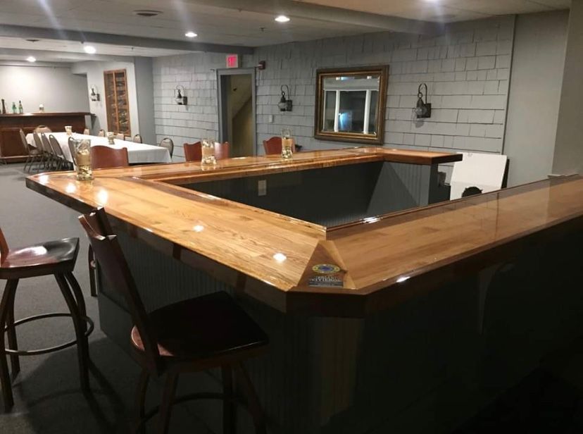 Empty basement bar with wooden countertop, black stools, and gray paneled walls