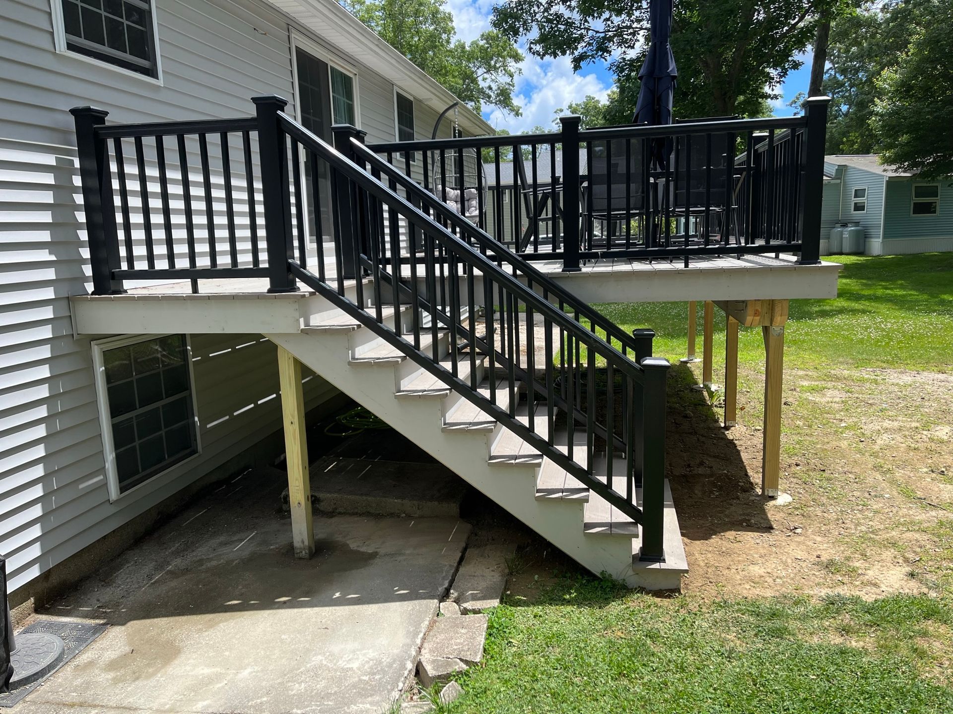 House deck with black railing and stairs leading to a concrete patio over a basement entrance