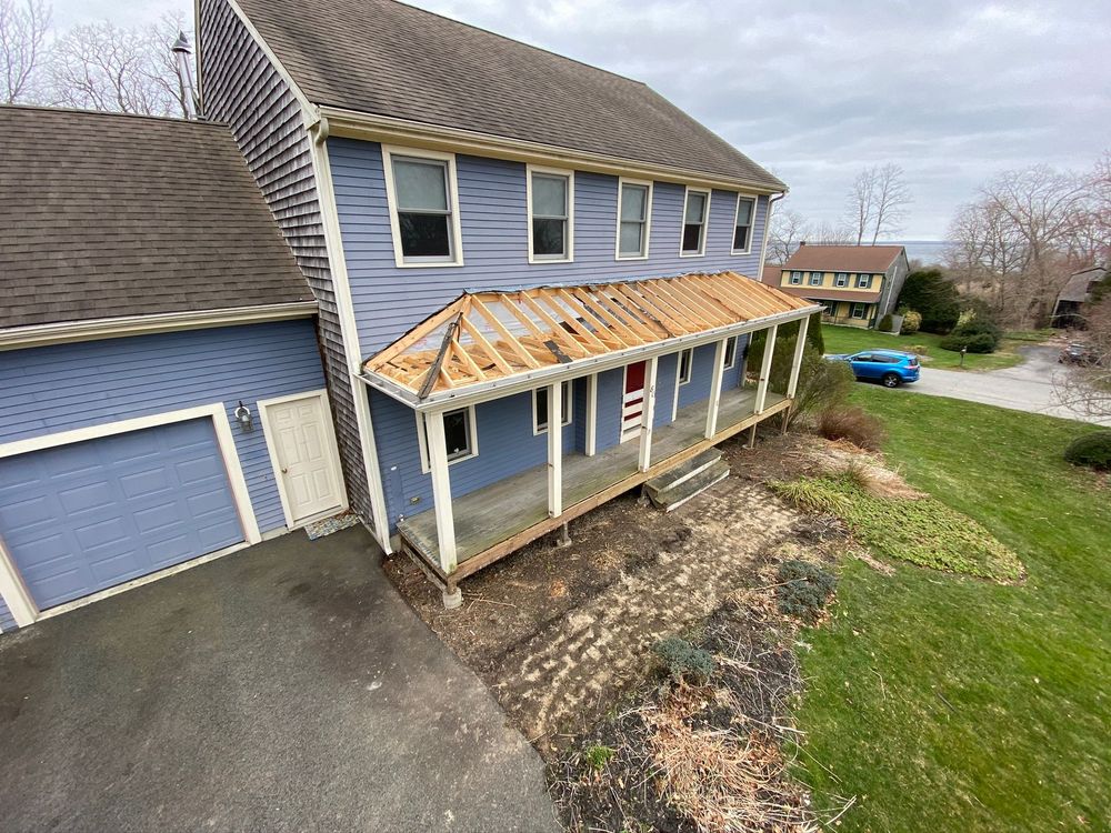 Damaged blue two-story house with a partially missing front porch roof and a driveway beside it