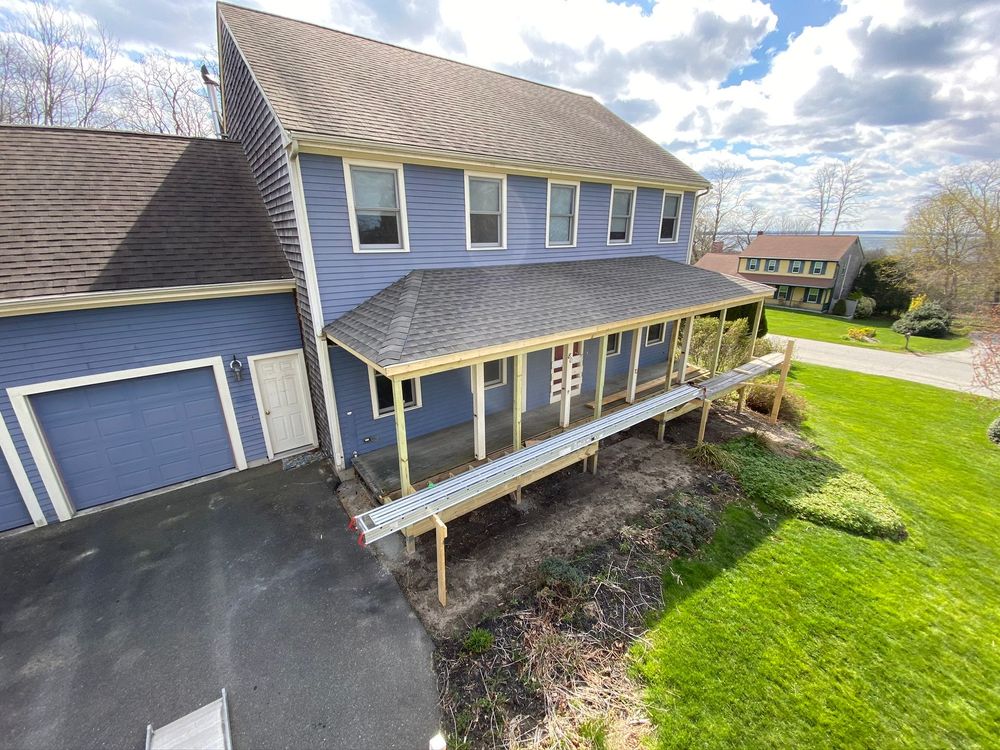 Two-story blue house with a front porch, garage, and green lawn under a partly cloudy sky