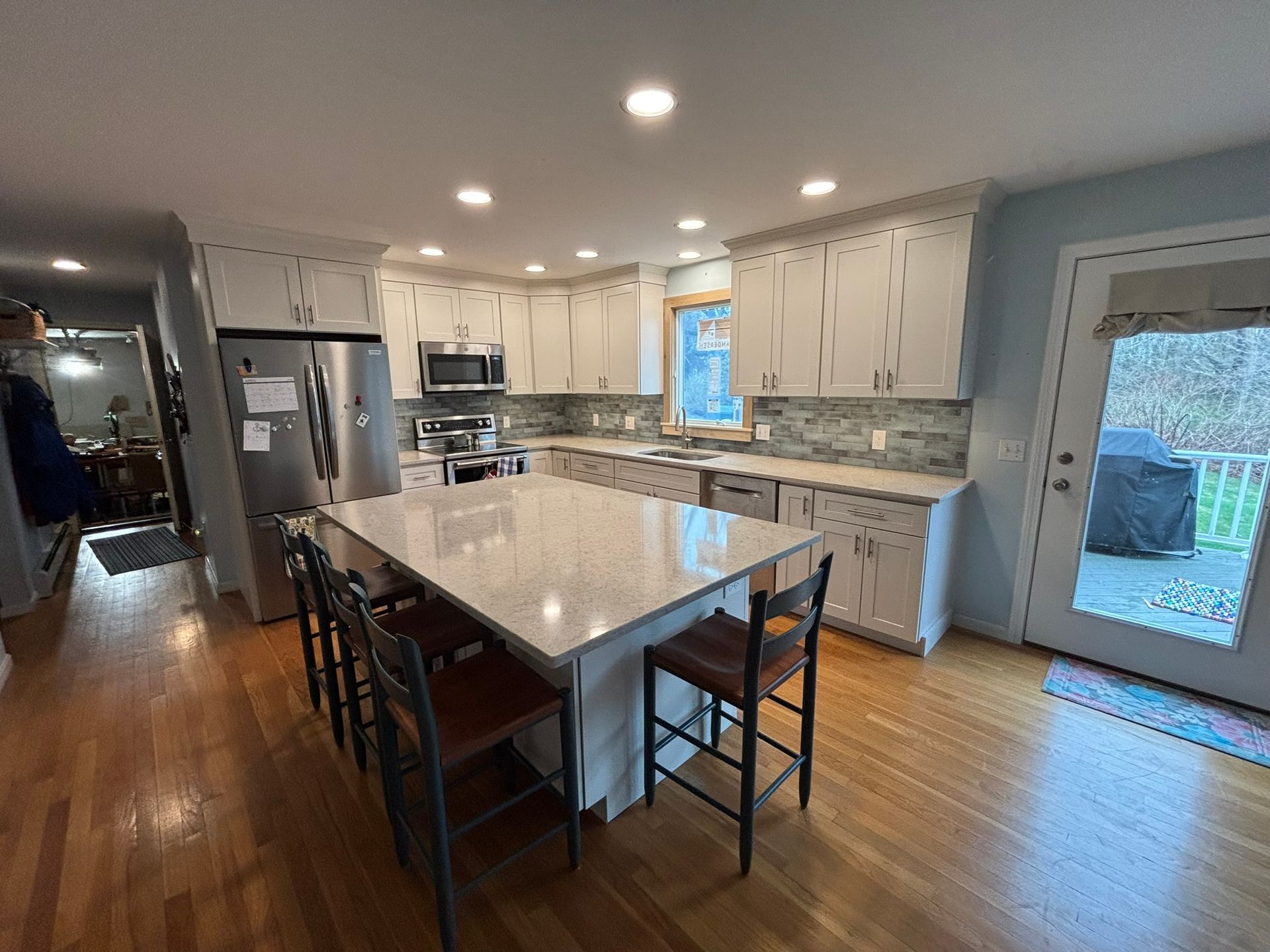 Bright modern kitchen with island, stainless appliances, white cabinets, and blue accent wall by glass door