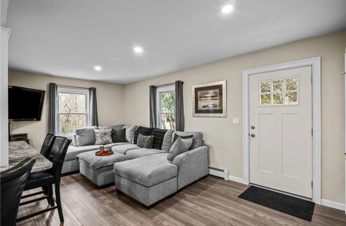 Cozy living room with gray sectional sofa, wall-mounted TV, hardwood floors, and white front door