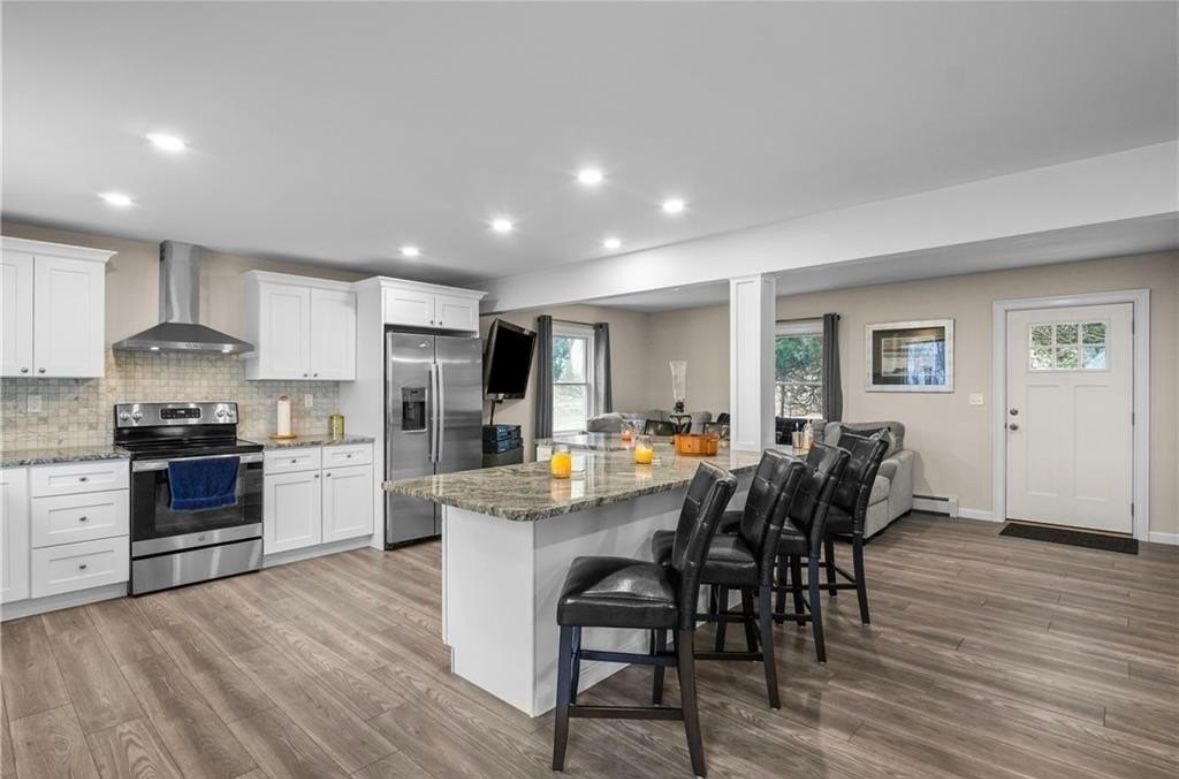 Modern open-concept kitchen with white cabinets, gray island, bar stools, and wood-look flooring