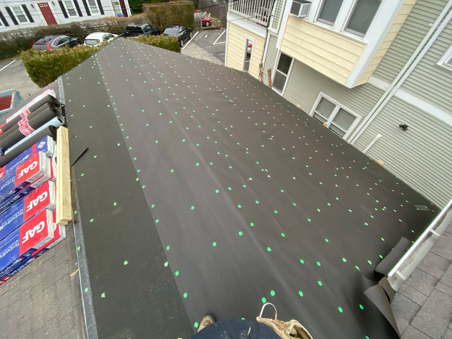 Roofing underlayment with rows of green fasteners on a sloped house roof, viewed from above