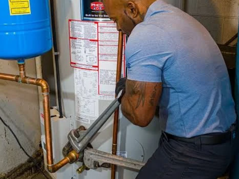 Plumber repairing copper pipes beside a blue water heater in a utility room