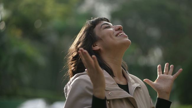 A woman is looking up at the sky with her hands in the air.