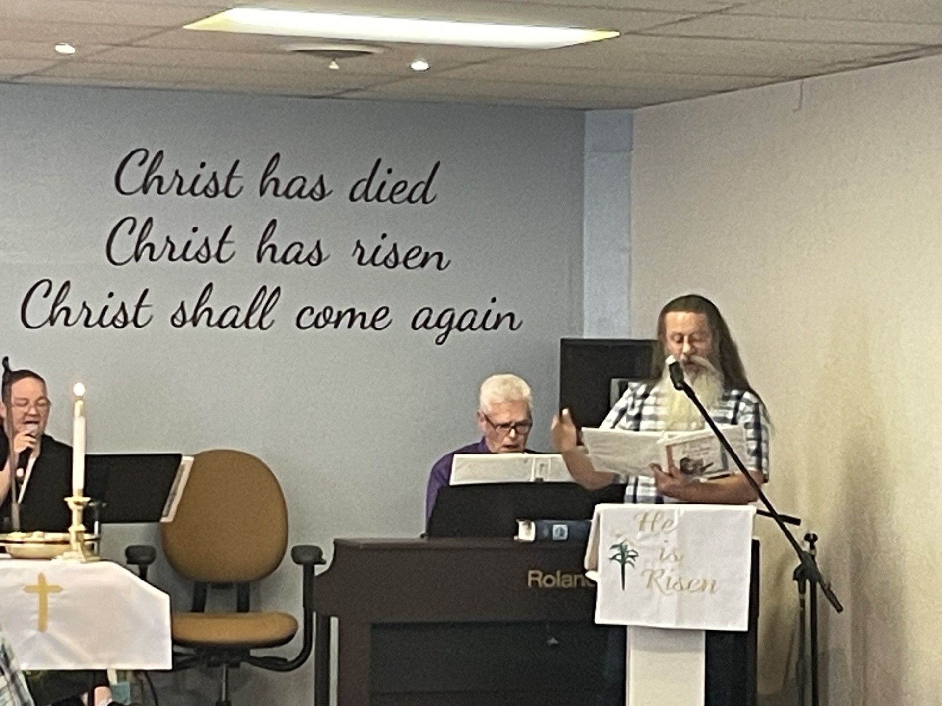 A man is giving a speech in front of a wall that says christ has died christ has risen christ shall come again