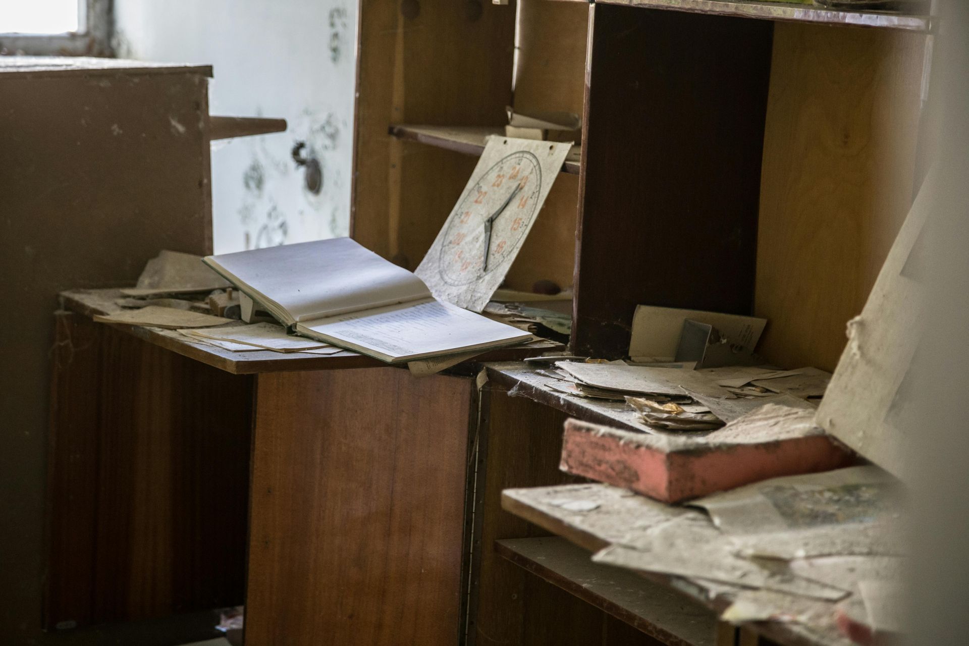 Abandoned room, desk with open book, clock, and debris. Dusty, brown tones, suggesting decay.