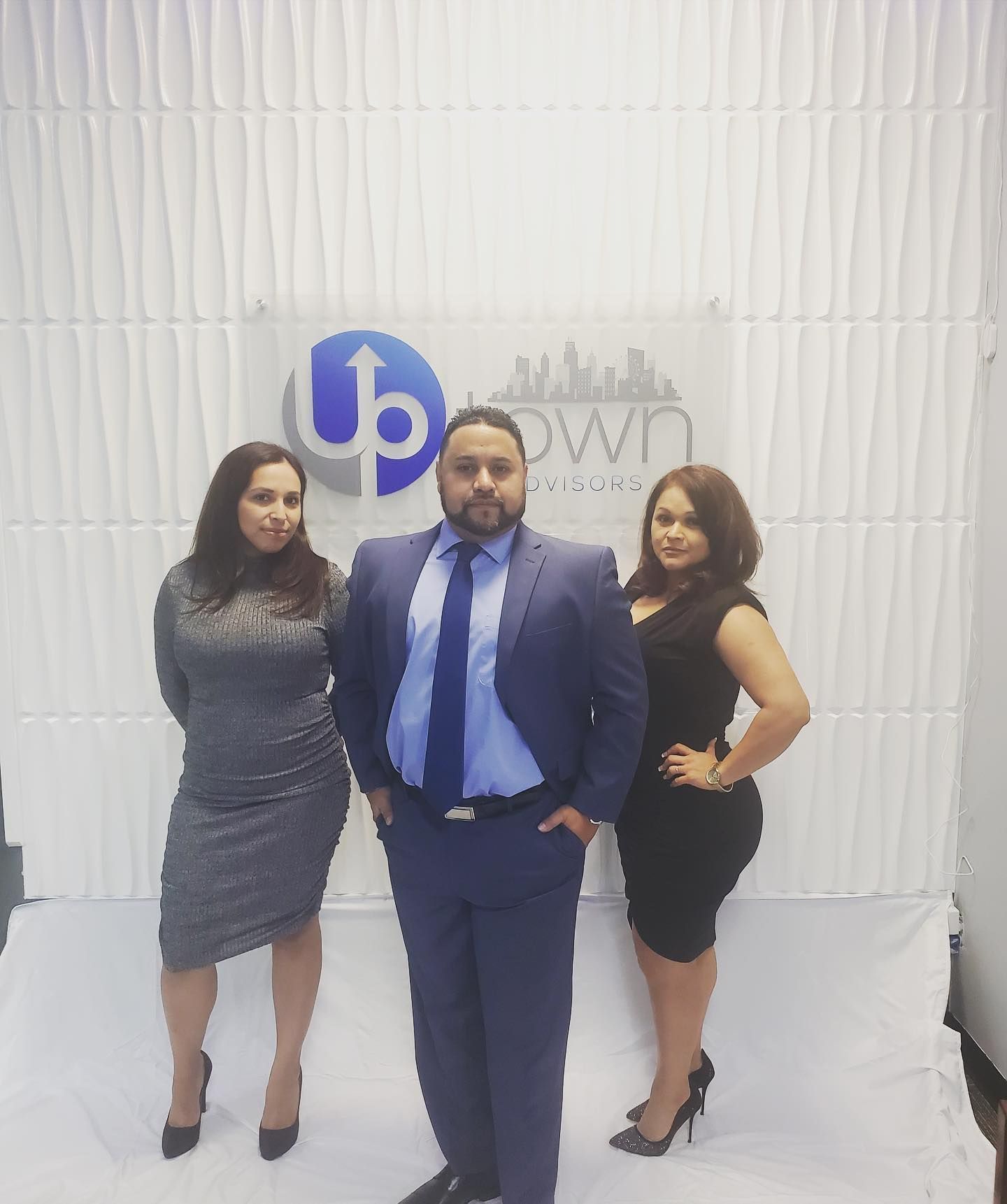 Three people stand in a line before an Uptown logo on a white, textured backdrop.