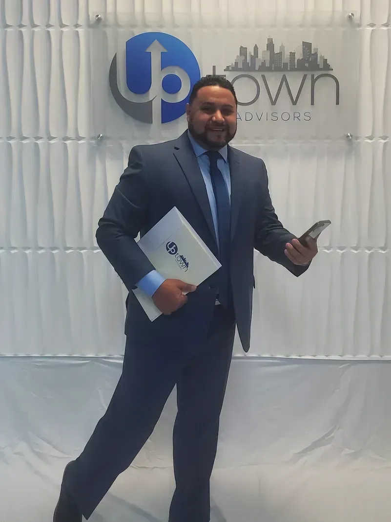 A smiling professional in a navy suit holding a folder and phone in front of an