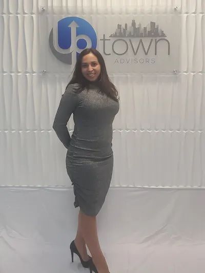 A person wearing a grey dress stands smiling in front of a wall sign that reads