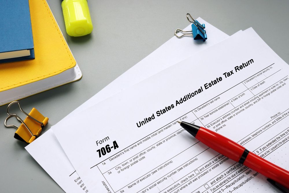 IRS Form 706-A (United States Additional Estate Tax Return) on a desk with a red pen, a yellow notebook, and binder clips.