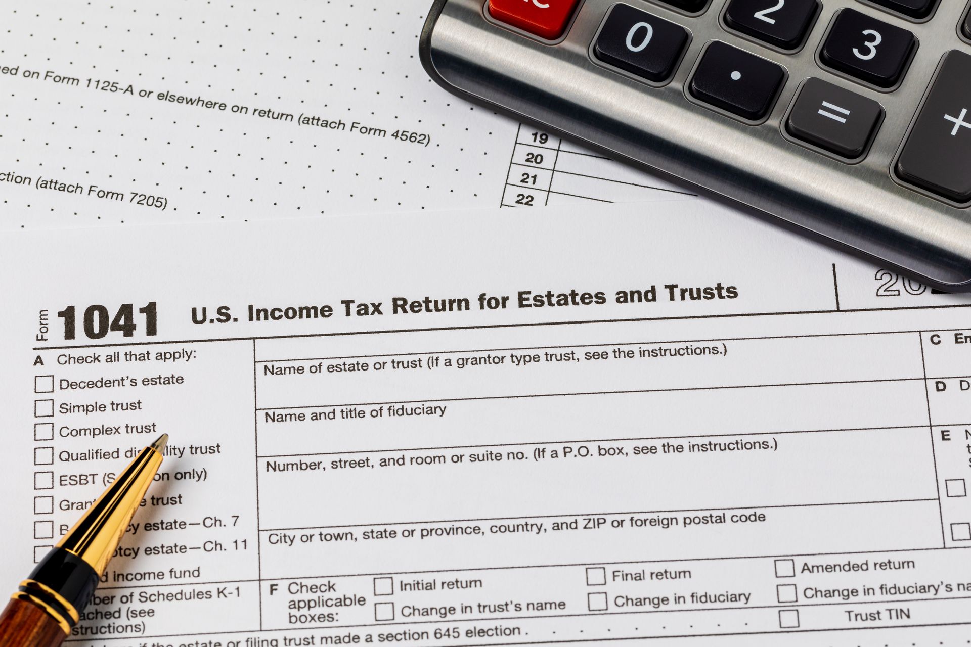 A U.S. Form 1041 income tax return for estates and trusts lies on a surface with a calculator and a fountain pen.